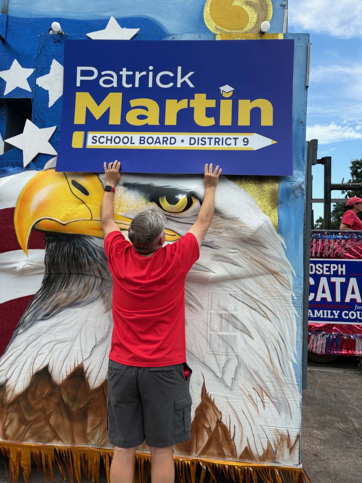 Charlie Davis lifts a large Patrick Martin campaign sign onto a patriotic float topped with an American bald eagle.